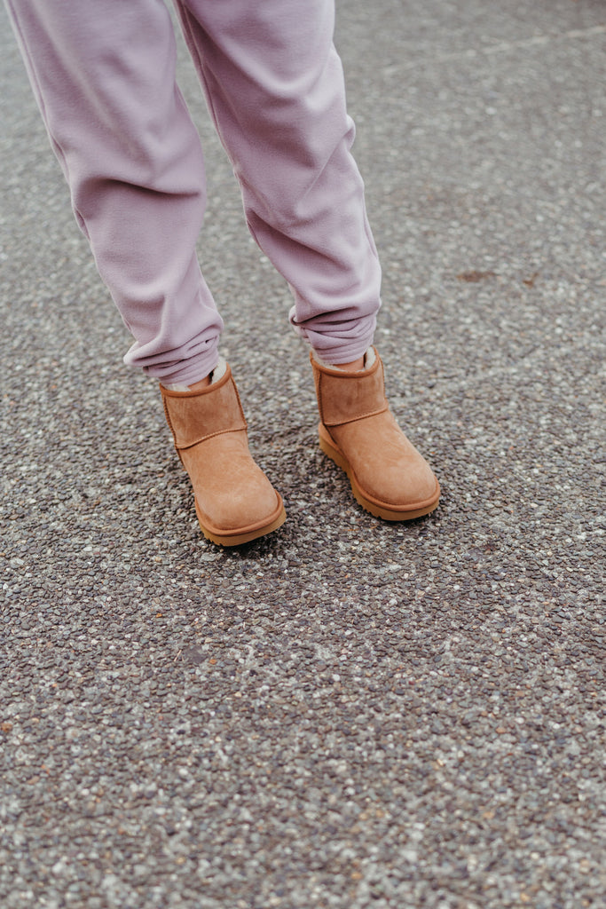 A woman in lavender sweatpants wearing beige Ugg boots. Seen from the thighs down,